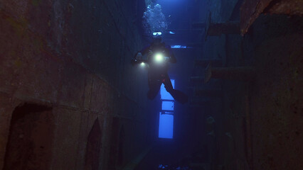 Scuba diver with lantern floats inside of ferry Salem Express shipwreck, Red sea, Safaga, Egypt