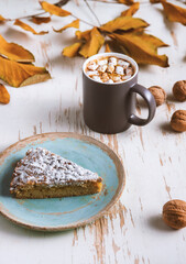 Top view of female hands holding marshmallows on shabby table with piece of cake, walnuts and scattered leaves, autumn composition
