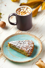 Top view of female hands holding marshmallows on shabby table with piece of cake, walnuts and scattered leaves, autumn composition