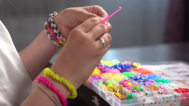 The girl's hands at the table knit rubber band bracelets with wicker tools