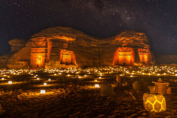 Starlight sky over the ancient nabataean tombs of Hegra city illuminated, night panorama, Al Ula, Saudi Arabia