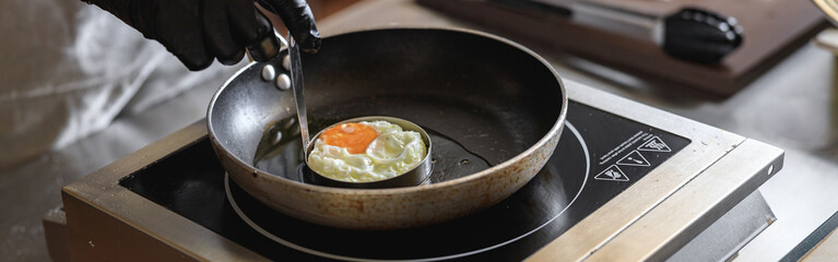 Professional kitchen worker cooking egg on a frying pan to make delicious breakfast