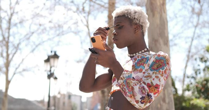 Focused black transgender person applying mascara on street