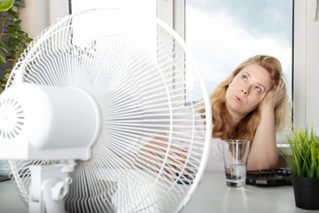 Woman in the office, feeling the refreshing airflow from a fan, summer heatwave - obrazy, fototapety, plakaty
