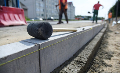 Concrete curbs are installed along the road, a hammer is on top.