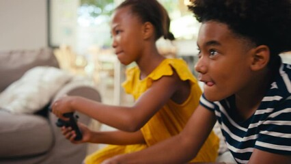 Brother and sister sitting on sofa at home holding controllers playing video game together  shot in slow motion