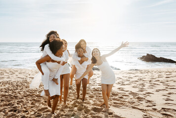 Female friends piggybacking each other at the beach, enjoying time together, cheerfully smiling and fooling around, free space