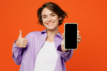 Young woman she wears purple shirt white t-shirt casual clothes hold in hand use close up mobile cell phone with blank screen workspace area show thumb up isolated on plain orange background studio.