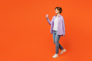 Full body young woman wear purple shirt white t-shirt casual clothes hold takeaway delivery craft paper brown cup coffee to go isolated on plain orange background studio portrait. Lifestyle concept.
