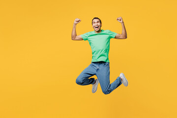 Fototapeta na wymiar Full body young man of African American ethnicity he wears casual clothes green t-shirt hat jump high doing winner gesture celebrate clenching fists say yes isolated on plain yellow background studio.
