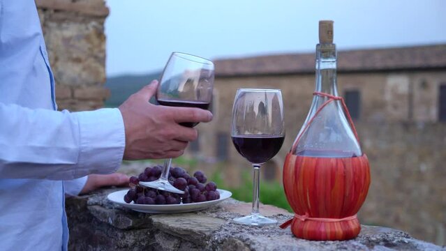 Man testing red wine from the typical chianti wine bottle fiasco against the backdrop of the Tuscany landscape