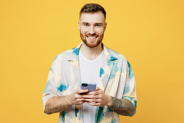 Young smiling happy cool fun man wear blue shirt white t-shirt casual clothes hold in hand use mobile cell phone isolated on plain yellow background studio portrait. Tattoo translates life is fight.