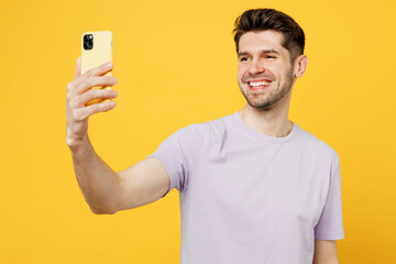Young smiling man he wear light purple t-shirt casual clothes doing selfie shot on mobile cell phone post photo on social network isolated on plain yellow background studio portrait Lifestyle concept