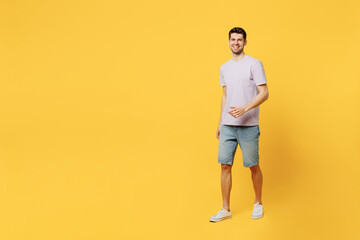 Fototapeta na wymiar Full body side view young cheerful fun happy smiling man he wear light purple t-shirt casual clothes walking going look camera isolated on plain yellow background studio portrait. Lifestyle concept.