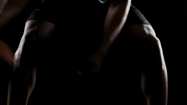 Basketball player bouncing a ball. African american sports man practicing against black background. Abstract body shot front view.