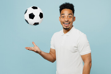Side view young happy man fan wear basic t-shirt look camera cheer up support football sport team hold in hand toss up soccer ball watch tv live stream isolated on plain pastel blue color background.