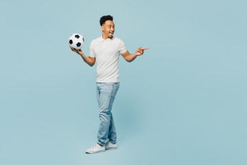 Fototapeta na wymiar Full body side view young man fan wear t-shirt cheer up support football sport team hold in hand soccer ball point index finger aside area watch tv live stream isolated on plain blue color background.