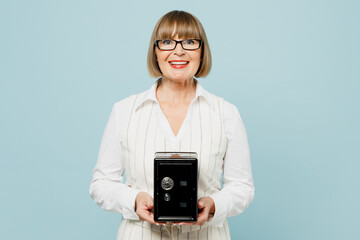 Happy employee business woman 50s wear white classic suit glasses formal clothes hold metal bank safe for money accumulation isolated on plain pastel light blue background. Achievement career concept.