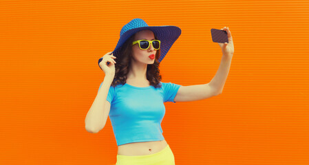 Stylish young woman 20s taking selfie with smartphone and blowing her lips wearing straw hat on...