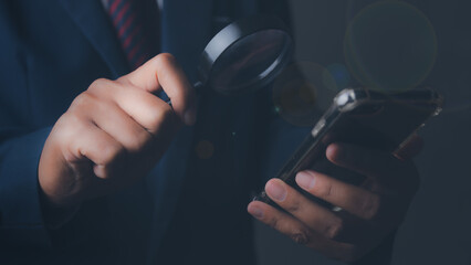 Businessman using magnifying glass and mobile smartphone searching data.