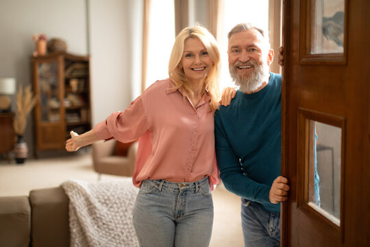 Happy Senior Couple Holding Opened Door Looking At Camera Indoor