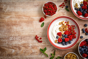 Yogurt with berries on wooden background. White plain greek yogurt with fresh berries and granola, top view. Healthy food, breakfast menu