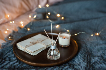 Liquid home fragrance in glass bottle with bamboo sticks with candle on tray over glow lights in bedroom close up.
