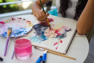 Woman painting watercolor drawing of asian girl with brush on a table with water and paints