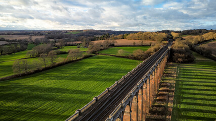Aerial photo of Ouse Valley Viaduct, a long and curved railway bridge spanning a lush green valley, surrounded by trees. © Daniel Caceiro