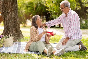 Cheerful senior european man gives present box to shocked glad woman, celebrate anniversary, birthday