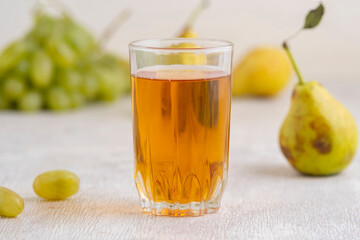 Juice of pears and grapes in a glass on a white wooden background