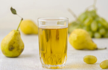 Juice of pears and grapes in a glass on a white wooden background