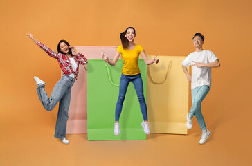 Asian customers celebrating shopping offer near large bags, orange background