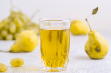 Juice of pears and grapes in a glass on a white wooden background