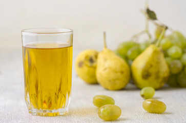 Juice of pears and grapes in a glass on a white wooden background