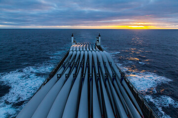Transportation of blades for wind turbines on a cargo ship across the ocean at sunset.