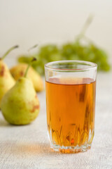 Juice of pears and grapes in a glass on a white wooden background