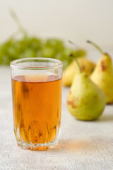 Juice of pears and grapes in a glass on a white wooden background