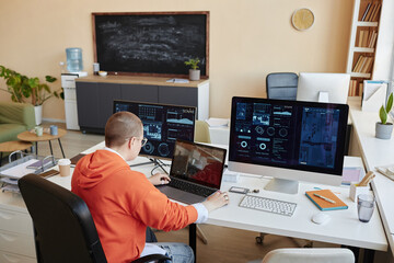 Female analyst or IT engineer sitting in front of computer monitor with illustration of development and fluctuations of cyber data on screen