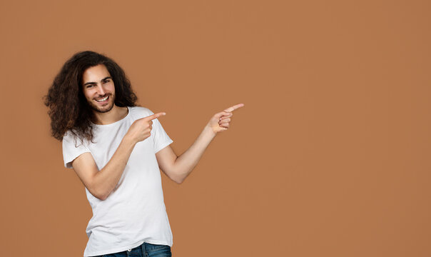 Happy Middle Eastern Young Man Pointing Fingers Aside, Brown Background
