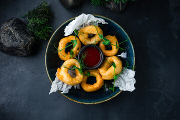 Breaded squid rings with sauce and microgreens on a dark background.
