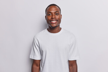 Horizontal shot of handsome smiling dark skinned man poses for making photo happy to have day off wears casual t shirt isolated over white background. People ethnicity and happy emotions concept