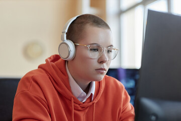 Young businesswoman in eyeglasses, red hoodie and headphones sitting in front of computer screen...