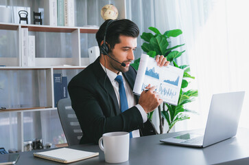 Business man wearing headphone present financial data or BI paper via laptop during online meeting. Remote work concept with virtual meeting presentation of effectiveness remote work. Fervent