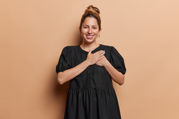 Thank you very much. Pleased young European woman with hair bun presses hands to chest expresses...