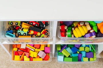 Transparent plastic storage boxs on shelves. White shelving with rainbow wooden toys in plastic containers. Toys sorting system. Organizing and storage ideas in nursery.
