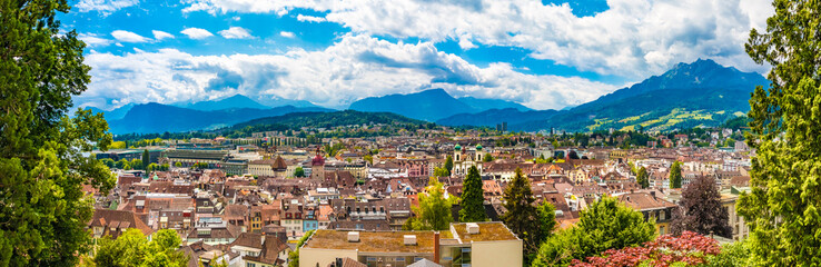 Fototapeta na wymiar Large panorama photo overlooking Lucerne's Old Town with an impressive mountainous panorama in the back, seen from the medieval fortification wall Museggmauer on a sunny day with a blue sky.