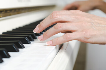 Obraz premium Close-up of female hands on piano keys. A woman with French manicure plays the piano. Musician with musical instrument learning music.
