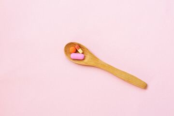 Top view variety of colorful vitamin and medicine pills in wooden spoon on pink background. Top view of assorted mineral pills.