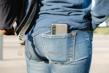Smartphone sticks out of the back pocket of jeans. The woman put her cell phone in the back pocket of her jeans. The concept of pickpocketing, indiscretion, frivolity. - obrazy, fototapety, plakaty